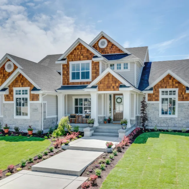 Front view of a modern suburban house with stone foundation, wooden shingle accents, and a manicured lawn pathway to the entrance.