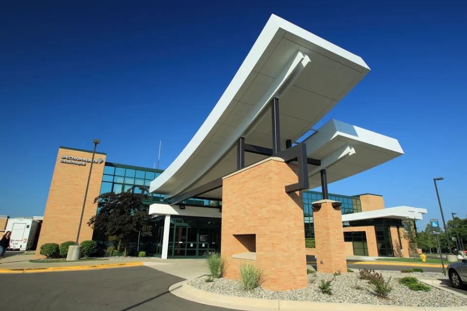 Modern building entrance with large curved white canopies supported by brick columns against a clear blue sky and glass façade behind.